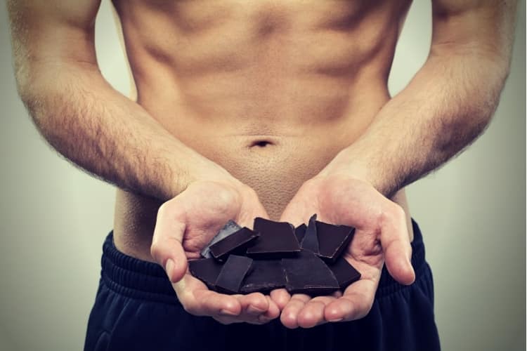 young fit man holding dark chocolate pieces young fit man holding dark chocolate pieces